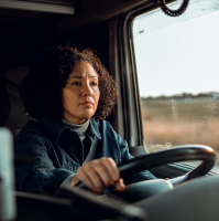 Women truck driver in her cab, holding the wheel with dry weather looking out the window. 